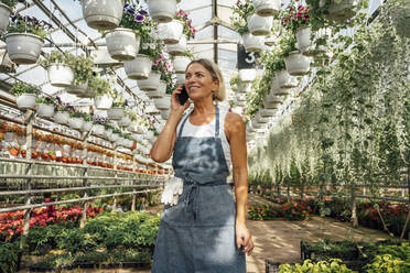 Smiling female agriculture worker talking on mobile phone in plant nursery - VPIF04670