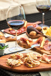 Delicious bacon served on wooden cutting board on table with various appetizers and glasses of red wine - ADSF29024