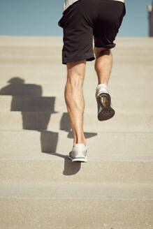 Back view of cropped unrecognizable athletic male running upstairs while training on sunny day in city in summer - ADSF29037