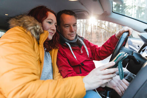 Seitenansicht von zwei Reisenden, die im Auto sitzen und während der Fahrt eine GPS-Karte auf dem Mobiltelefon benutzen - ADSF29065