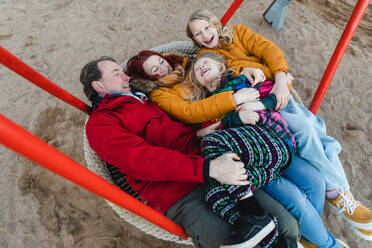 Von oben auf einer Netzschaukel auf einem Spielplatz im Herbstpark reitende Familie, die gemeinsam Spaß hat - ADSF29068