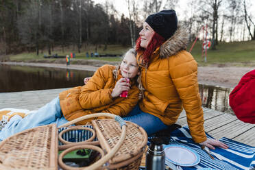 Loving family with teenage daughter relaxing on wooden quay and enjoying picnic in autumn forest - ADSF29069