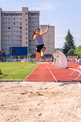 Full body of determined young female track and field athlete jumping during training on sports field - ADSF29073