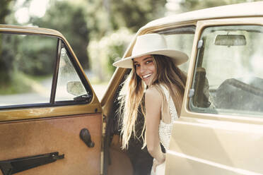 Smiling beautiful woman looking over shoulder while sitting in car - DGOF02272