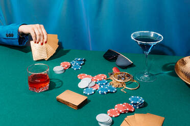 Crop unrecognizable female with cards and chips playing poker while sitting at green table - ADSF29129