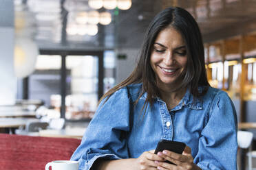 Lächelnde schöne Geschäftsfrau Textnachrichten über das Mobiltelefon, während sie im Café sitzt - PNAF02115