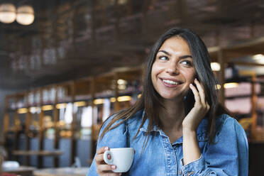 Smiling female freelancer talking on mobile phone at cafe - PNAF02116