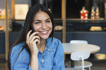 Schöne weibliche Freiberuflerin lächelnd während des Gesprächs auf dem Smartphone im Cafe - PNAF02118