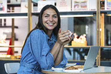 Lächelnde Frau mit Laptop bei einem Kaffee im Café - PNAF02121