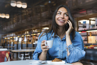 Geschäftsfrau mit Kaffeetasse, die lächelt, während sie mit einem Smartphone in einem Café spricht - PNAF02134