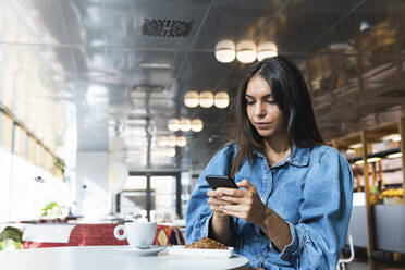 Junge Geschäftsfrau arbeitet in einem Café an einem Mobiltelefon - PNAF02136