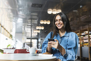 Beautiful businesswoman with mobile phone sitting at coffee shop - PNAF02137