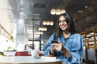 Schöne Geschäftsfrau mit Mobiltelefon in einem Café sitzend - PNAF02137