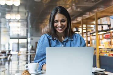 Lächelnde Geschäftsfrau, die in einem Café am Laptop arbeitet - PNAF02141