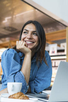 Schöne Geschäftsfrau mit Hand am Kinn, die sich auf einen Tisch in einem Café stützt - PNAF02146