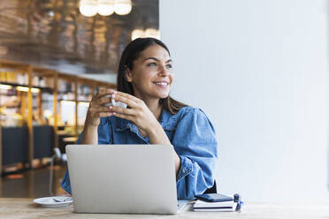 Smiling female freelancer with laptop having coffee at cafe - PNAF02148