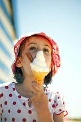 Girl looking away while eating ice cream in sunlight - AJOF01629
