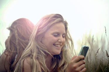 Glückliches Mädchen mit Smartphone und Freund im Hintergrund im Urlaub - AJOF01637