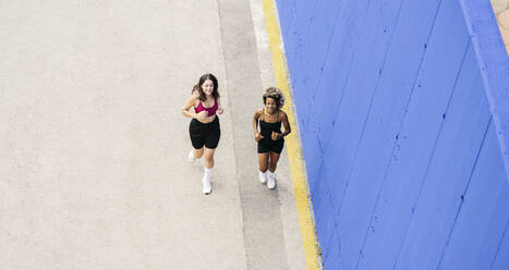 Smiling female friends running together on footpath - JCCMF03628