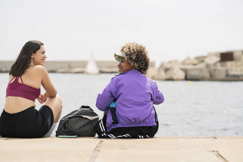 Lächelnde erwachsene Frauen, die sich beim Sitzen auf der Promenade ansehen - JCCMF03630