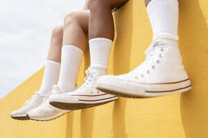 Mittlere erwachsene Frauen mit weißen Sportschuhen auf gelber Stützmauer - JCCMF03647