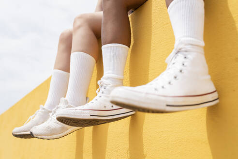 Mid adult women wearing white sports shoes on yellow retaining wall - JCCMF03647