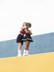 Lächelnde multiethnische Freundinnen stehen auf einer gelben Stützmauer - JCCMF03656