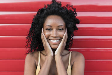Beautiful smiling woman with head in hands in front of red shutter - JRVF01652