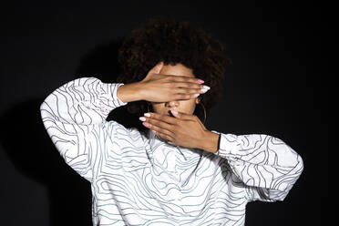 Woman covering eyes and mouth with hands against black background - GIOF13279