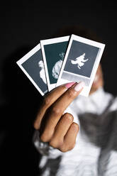 Frau zeigt Polaroidfotos vor schwarzem Hintergrund - GIOF13306