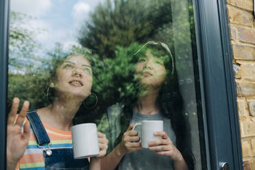 Young multi-ethnic female friends with coffee cup looking through glass window - ASGF01215