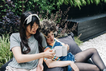 Friends toasting coffee cups while sitting on bean bag - ASGF01218