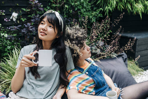 Junge Freunde mit Kaffeetassen entspannen sich auf einem Sitzsack im Hinterhof - ASGF01219