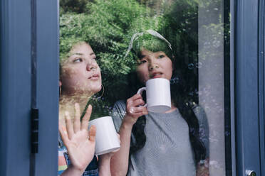 Friends having coffee while looking through house window - ASGF01240