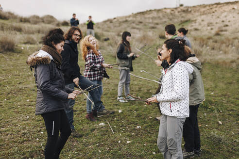 Male and female friends playing with sticks in field - MRRF01394