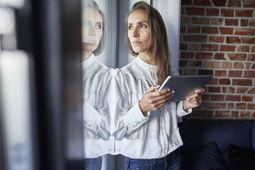 Geschäftsfrau mit digitalem Tablet, die durch ein Fenster zu Hause schaut - ABIF01468