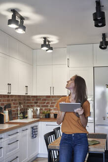 Woman controlling lights through digital tablet at home - ABIF01482