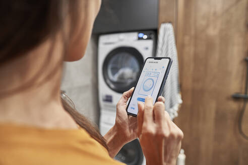 Woman operating washing machine through mobile application at home - ABIF01486