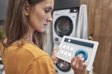 Woman using digital tablet to operate washing machine at home - ABIF01487