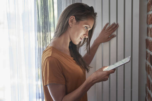 Woman checking temperature of radiator through digital tablet at home - ABIF01503