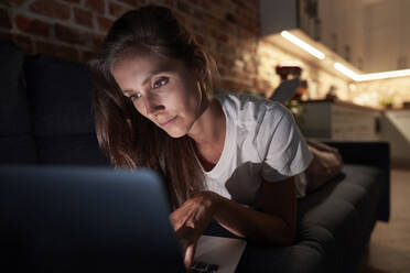 Woman using laptop on sofa at home during night - ABIF01512