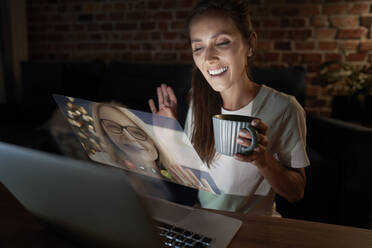 Woman waving while doing video call with mother at home - ABIF01516