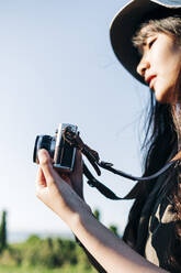 Junge Frau mit Hut beim Fotografieren durch die Kamera an einem sonnigen Tag - ASGF01245