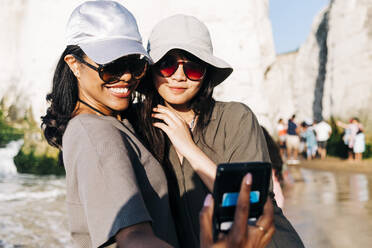 Happy woman taking selfie with female friend at beach during vacation - ASGF01247