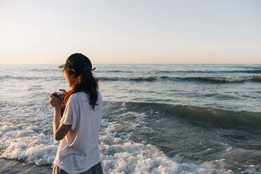 Junge Frau mit Kamera schaut im Urlaub aufs Meer - ASGF01255