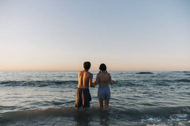 Young male and female friends looking at sea during sunset - ASGF01263