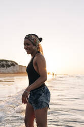 Lächelnde Frau hat Spaß am Strand bei Sonnenuntergang - ASGF01264