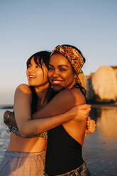 Smiling female friends embracing at beach - ASGF01268