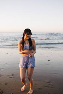 Lächelnde junge Frau hat Spaß am Strand bei Sonnenuntergang - ASGF01274