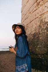 Schöne junge Frau mit Mobiltelefon am Strand stehend - ASGF01279